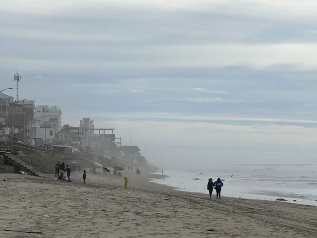 People walking beside the ocean with buildings lining the Tijuana beachfront.