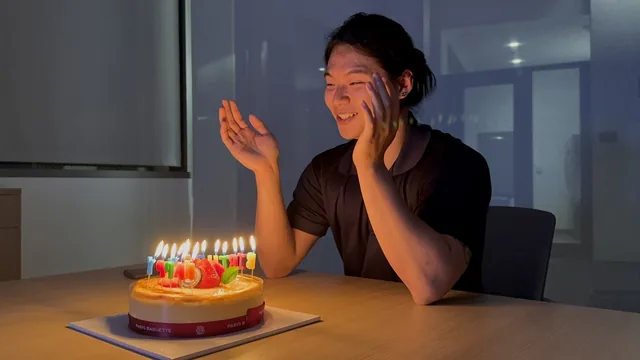 Smiling beside a birthday cake lit with candles.