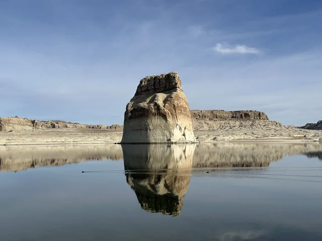 Lone Rock reflected in still water beneath a blue sky.