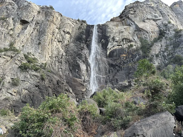 A waterfall descending a granite cliff above trees and boulders in Yosemite.